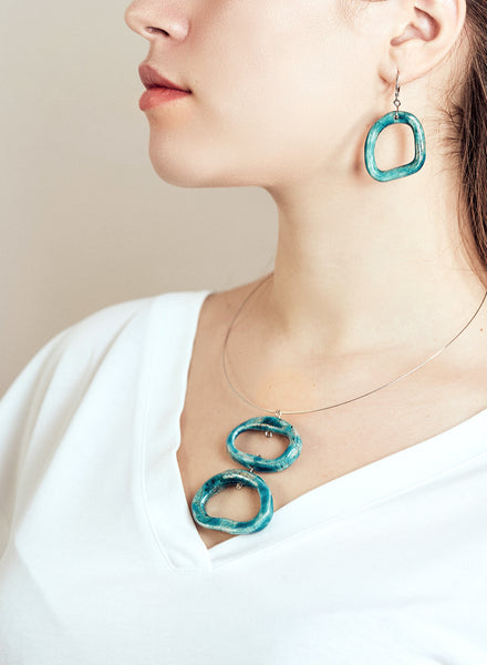 Collana Ojos con pendenti ovali in ceramica Raku con sfumature turchesi e girocollo in acciaio