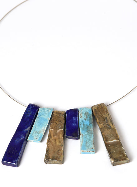 Collana in ceramica Raku con strisce verticali nei toni dell’oro, dell’azzurro e del blu profondo. 