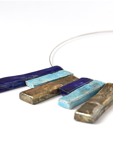 Collana in ceramica Raku con strisce verticali nei toni dell’oro, dell’azzurro e del blu profondo. 