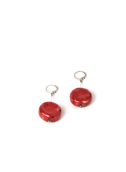 Orecchini artigianali con pendente lungo in acciaio e disco rosso in ceramica Raku, montati su un gancio rotondo.