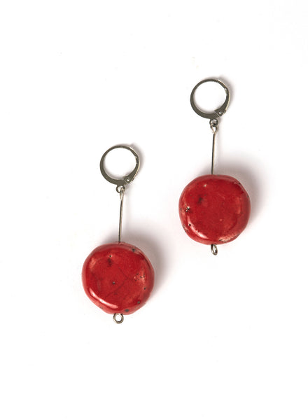 Orecchini artigianali con pendente lungo in acciaio e disco rosso in ceramica Raku, montati su un gancio rotondo.