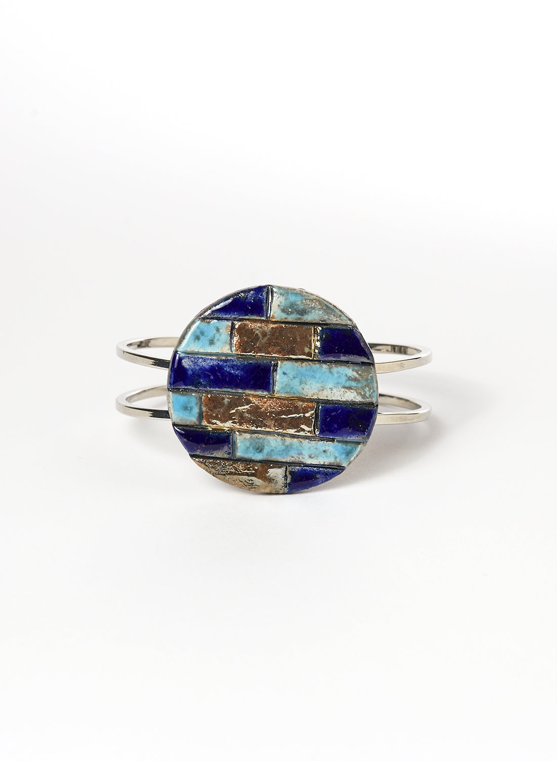Bracciale rigido in metallo lucido con elemento in ceramica Raku, caratterizzato da un disco decorato con inseriti a rilievo in tonalità marine: blu, turchese e oro. 