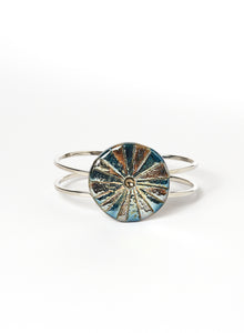 Bracciale rigido in lega con elemento in ceramica Raku, caratterizzato da un disco con luminose striature dorate.