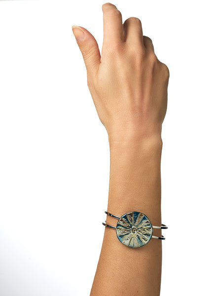 Bracciale rigido in lega con elemento in ceramica Raku, caratterizzato da un disco con luminose striature dorate.